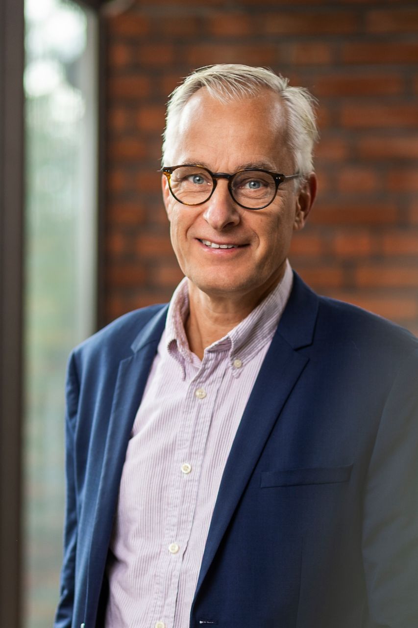 Magnus Jalkesten, head of regulatory affairs at TRATON GROUP R&D, standing in front of a brick wall wearing a light purple shirt and blue blazer. 
