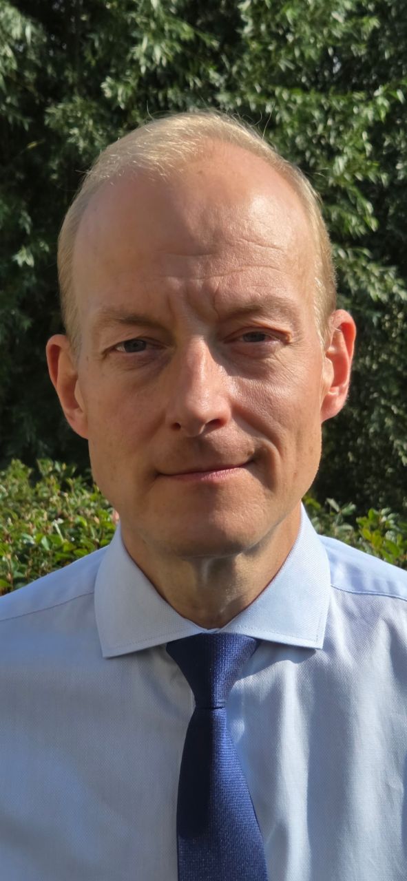 Reimert Sjöblom, Product Property Manager - safety at Scania, in front of green leafs wearing a blue shirt and blue tie. 