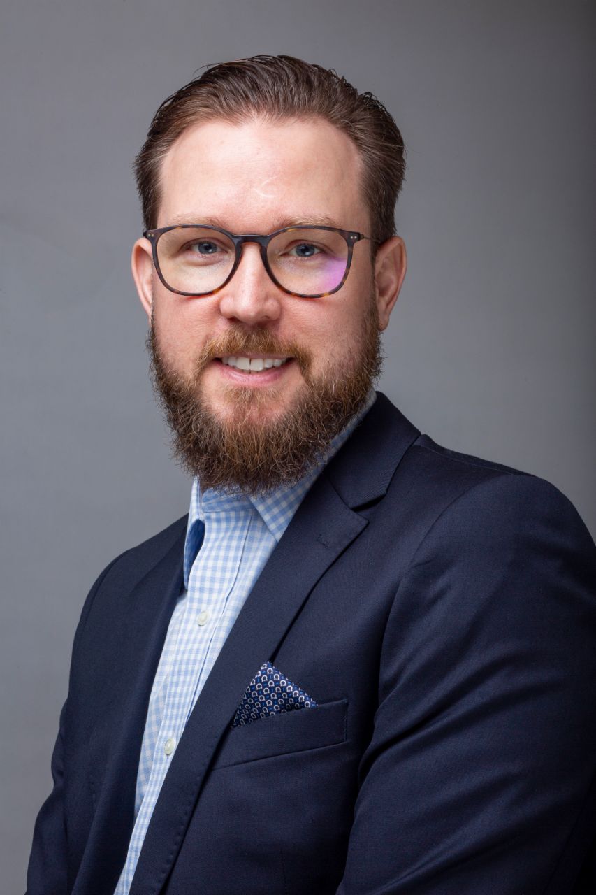 Huber Mastelari, VP Service Contracts & Connectivity bei International, mit Brille, blauem Hemd und marineblauem Mantel. 