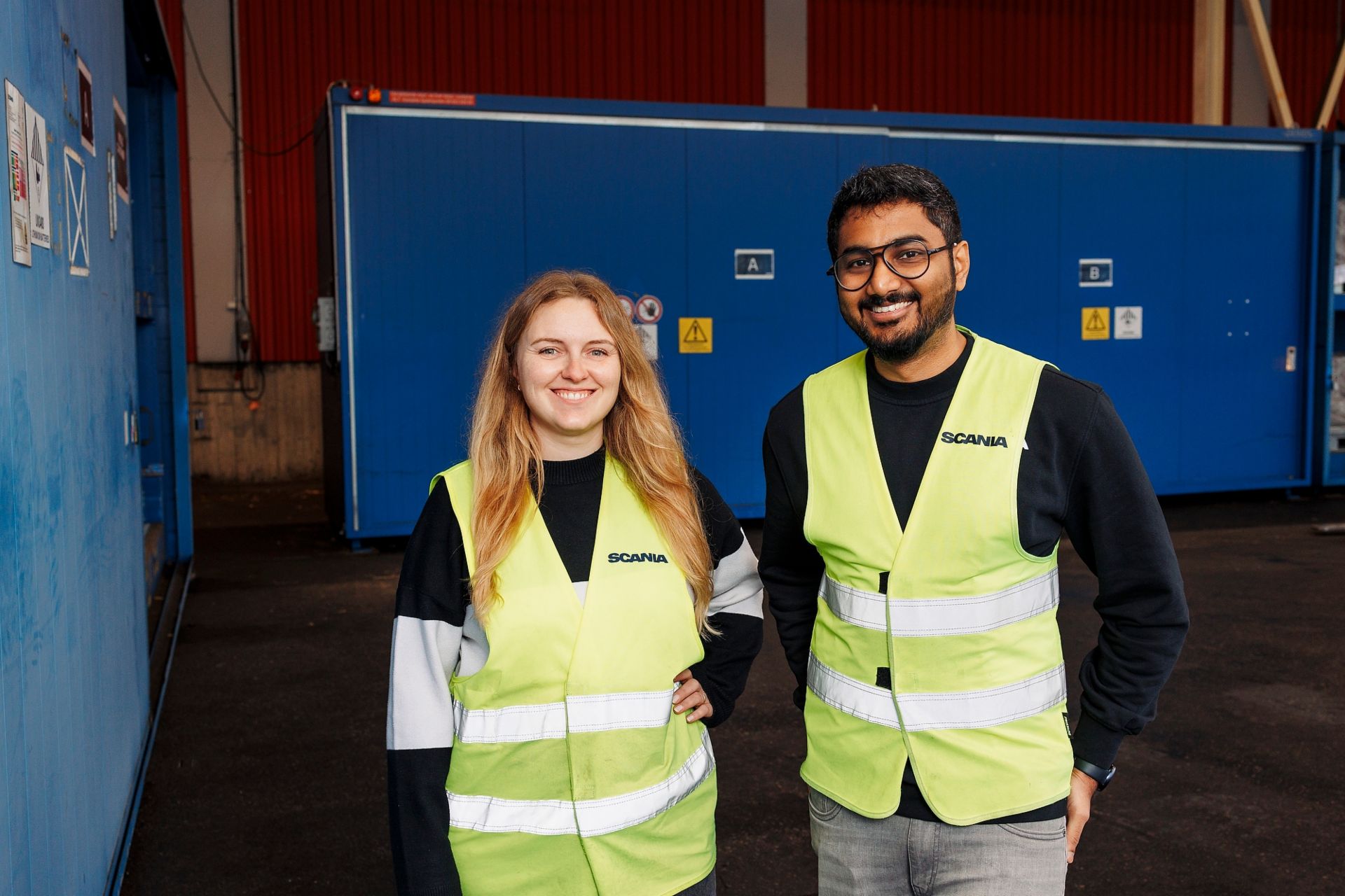 Die Batterieproduktionsingenieure Christina Brunhardt (MAN) und Aswin Ravikumar (Scania) tragen gelbe Sicherheitswesten in einem Batterielager. Sie gehören zum Team, das Produktionslösungen für zukünftige Batterieplattformen entwickelt. 